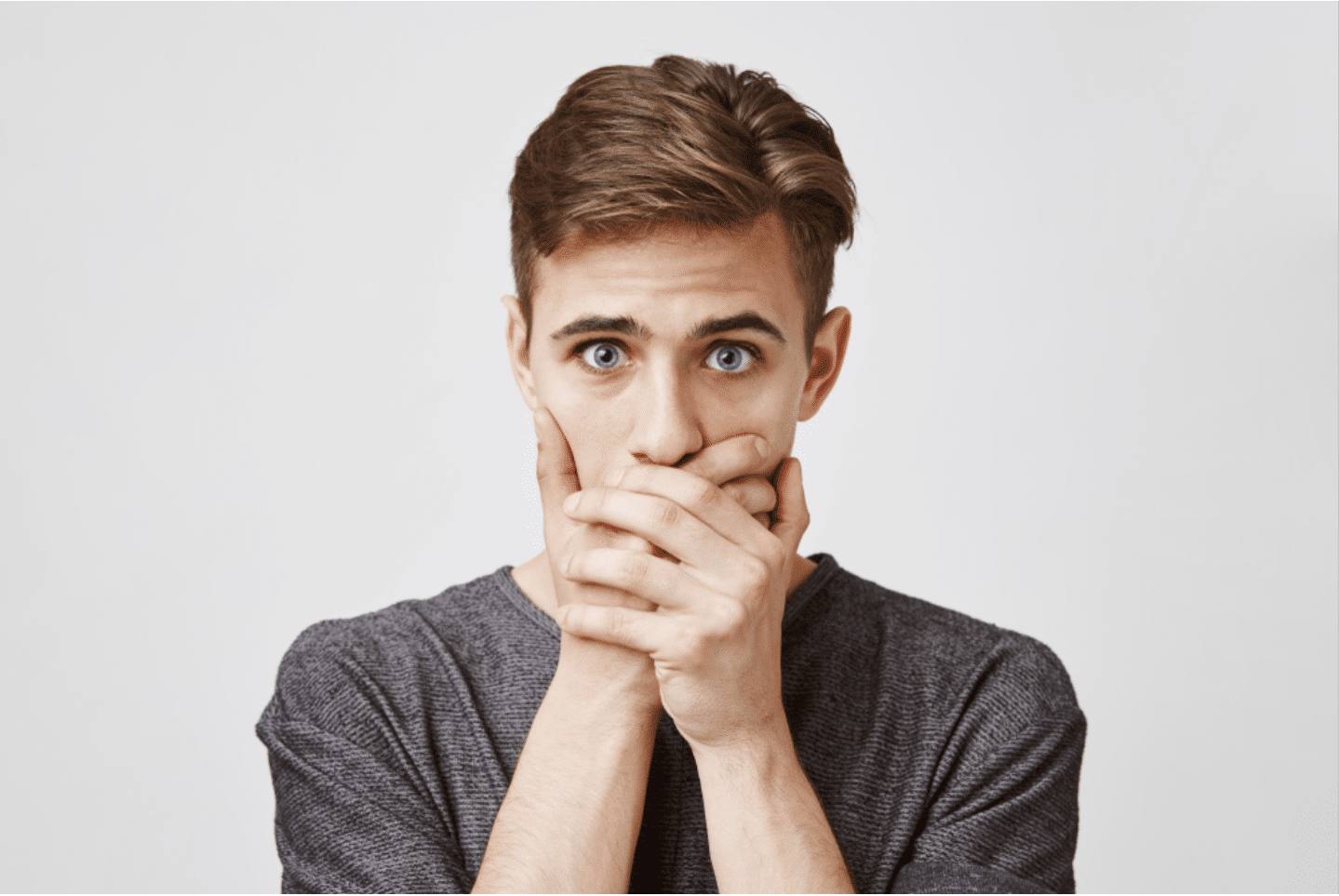 a young man anxious about the cause of his bad breath; he is covering his mouth