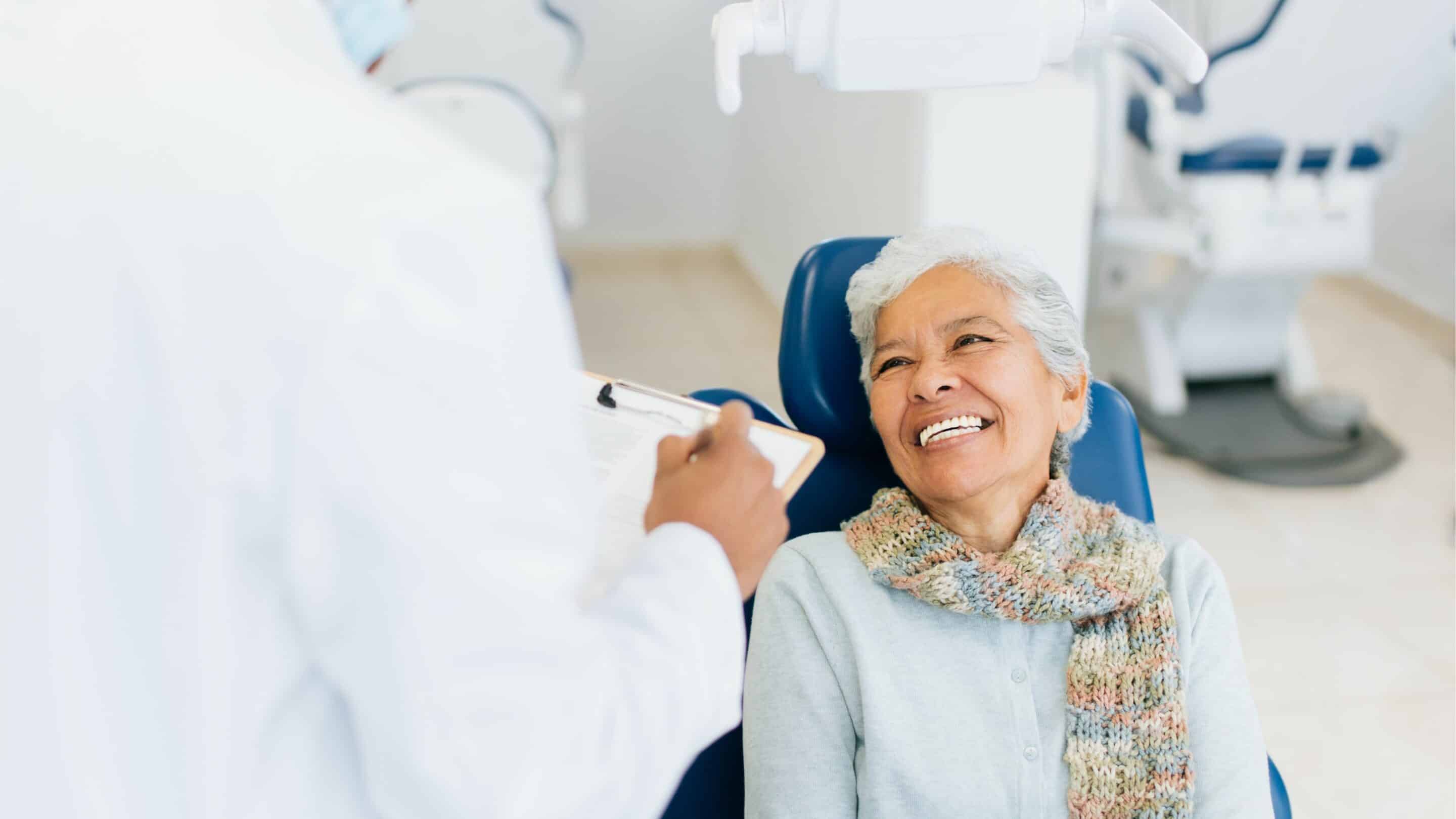 Smiling senior woman in dental chair receiving care from dentist in white coat