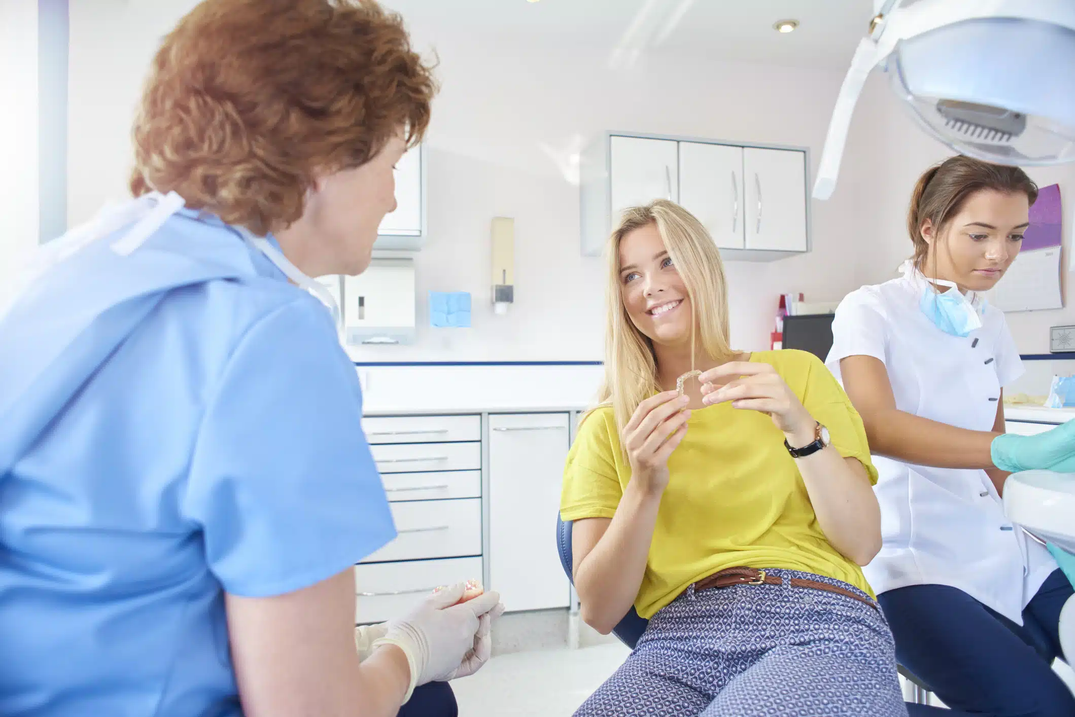 Woman holding Invisalign clear aligners talking to dentist.