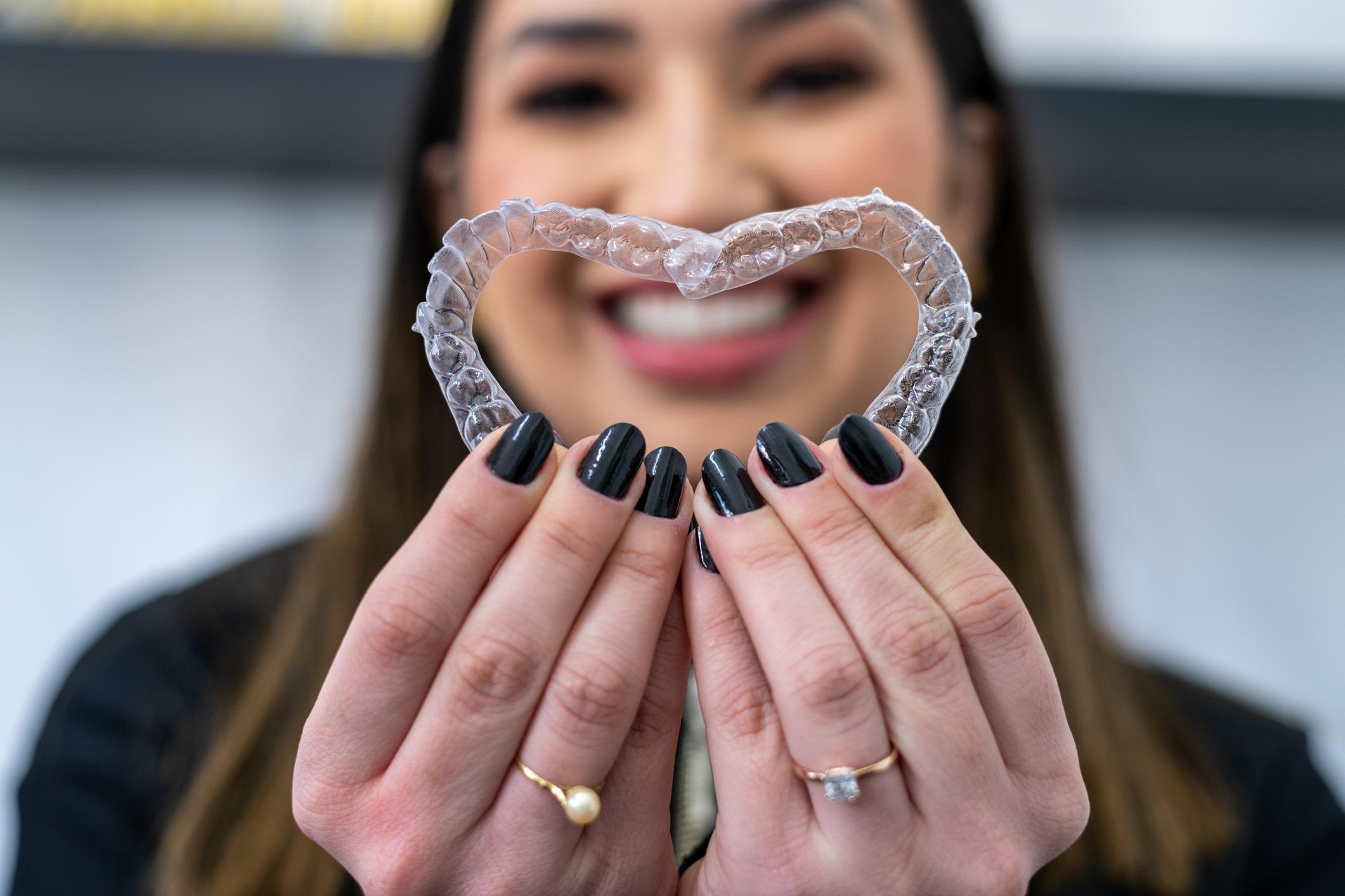 Woman smiling and holding Clear Aligners/Invisible braces forming a heart shape.