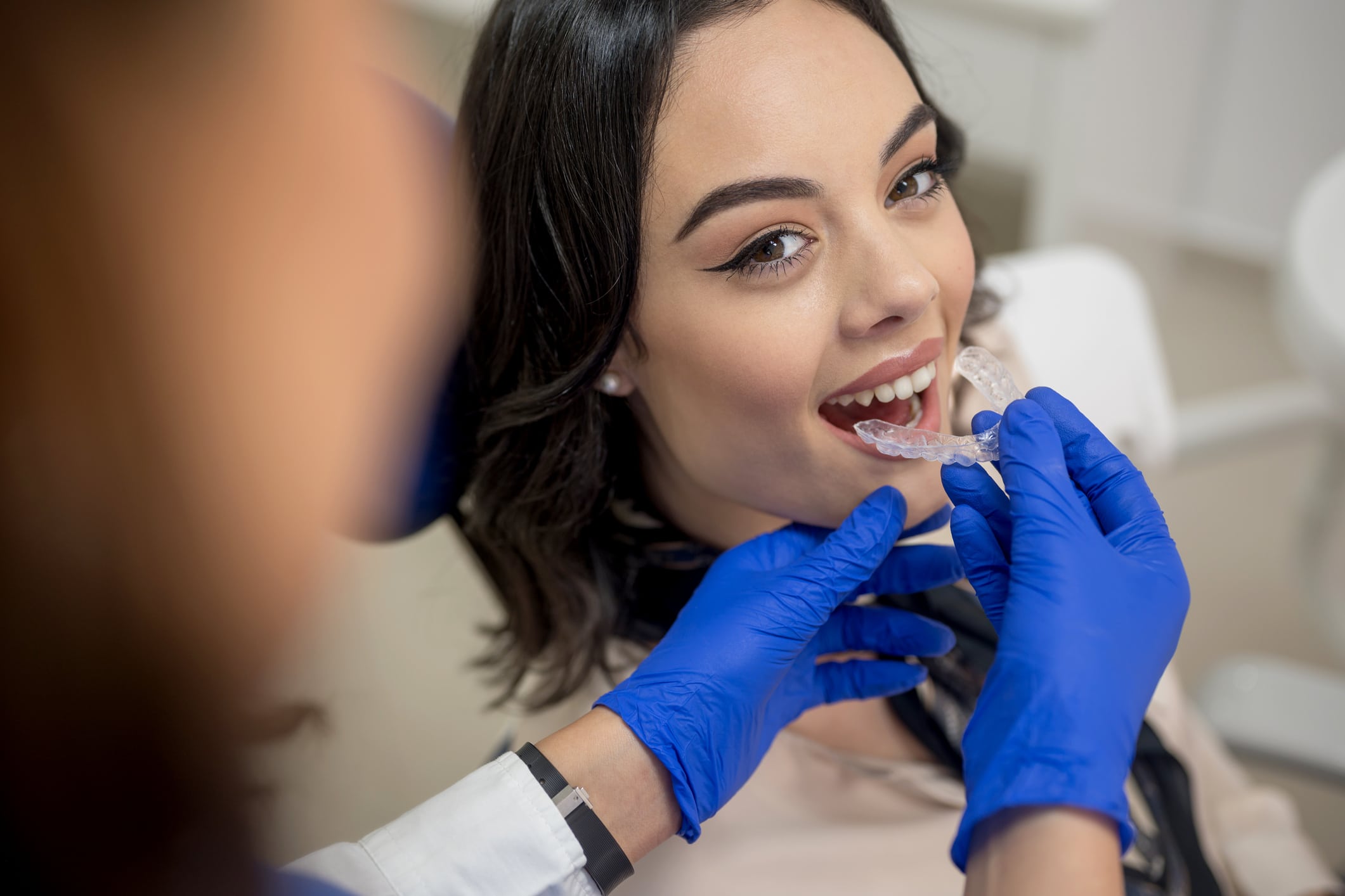 Invisalign clear aligners being placed in woman's mouth by dentist.