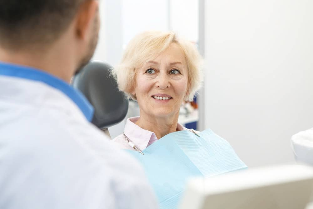 an old woman seated on a dental chair for a dental procedure for her missing toothh