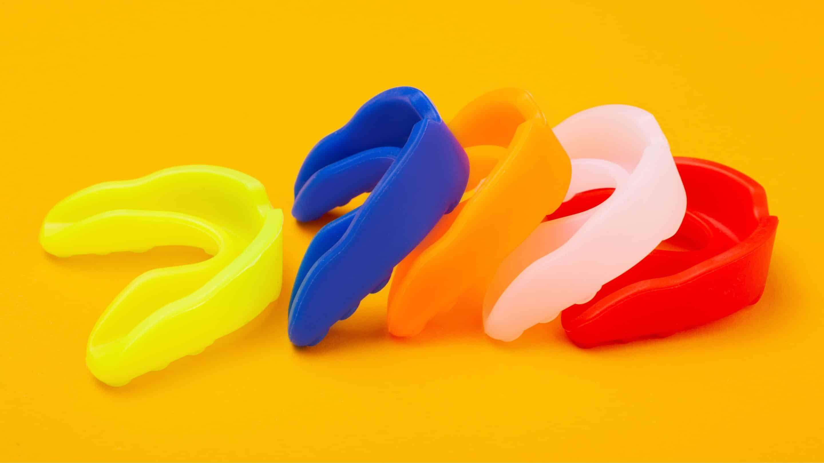 Different coloured dental sports mouthguards on a yellow background.