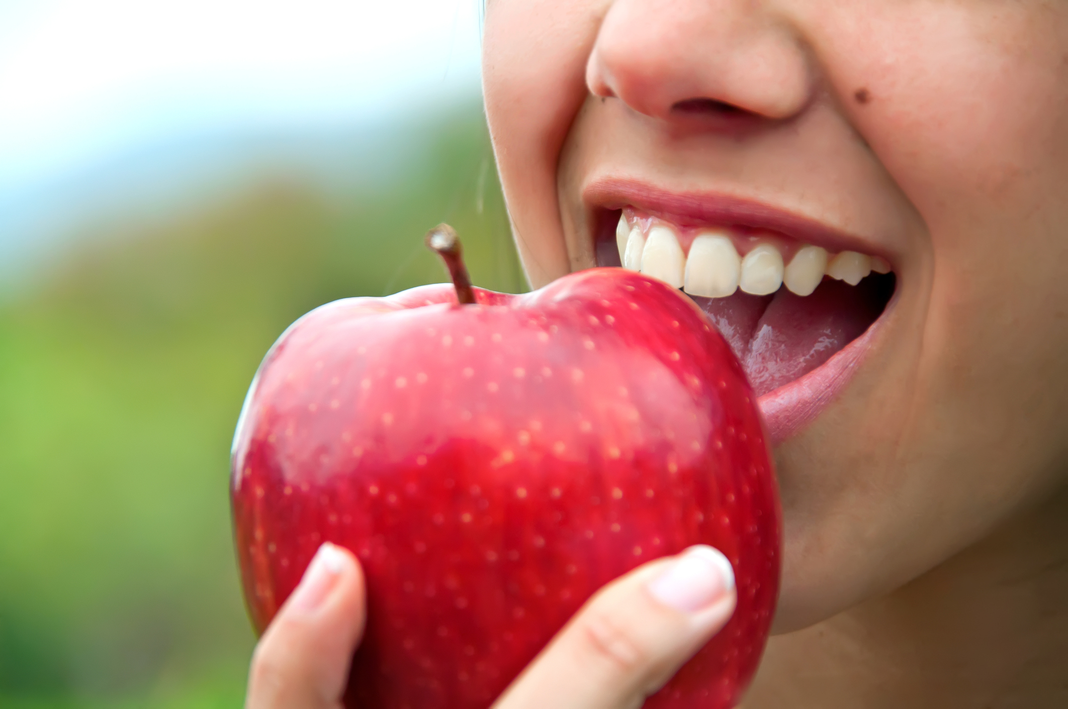 A close-up of female smiling and eating a red apple showcasing the link between diet and oral health.