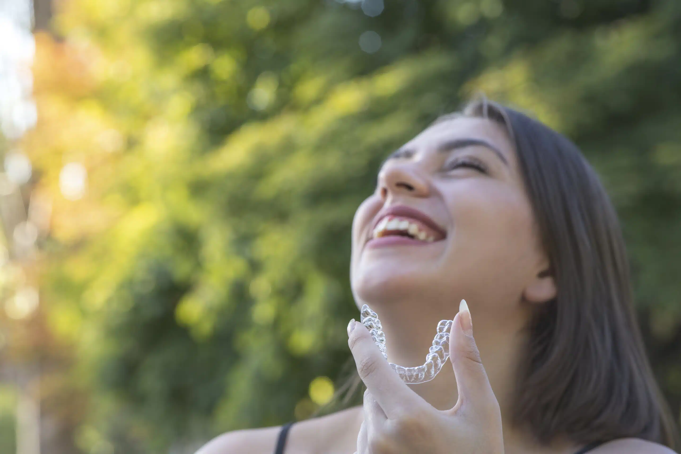 Woman smiling holding her Invisalign clear aligners in left hand.