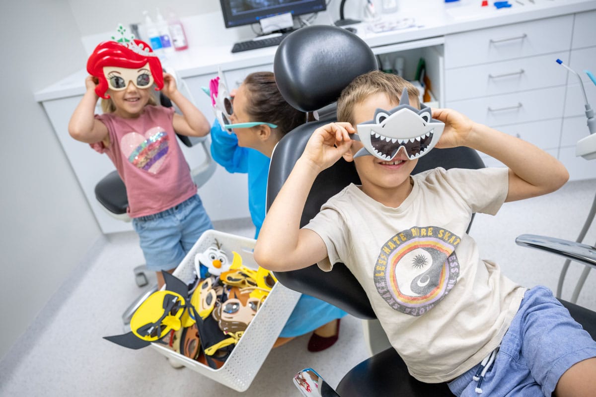 Two children at the dentist smiling and trying on toy glasses