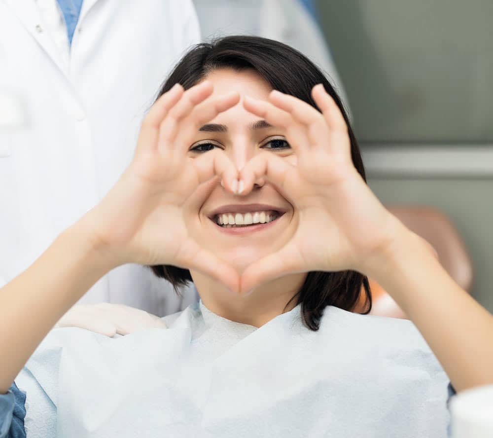 a happy patient with her hands in the air and shaped like a heart because she has multiple options for her missing teeth in Beaches Dental