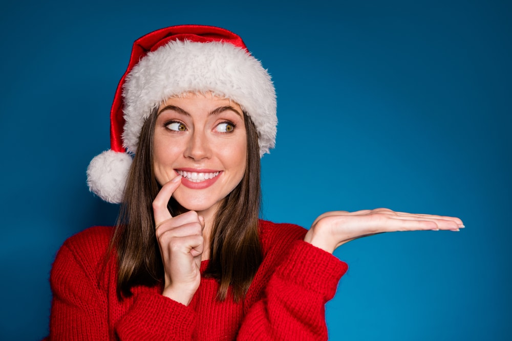 a woman with a santa hat pointing at her teeth