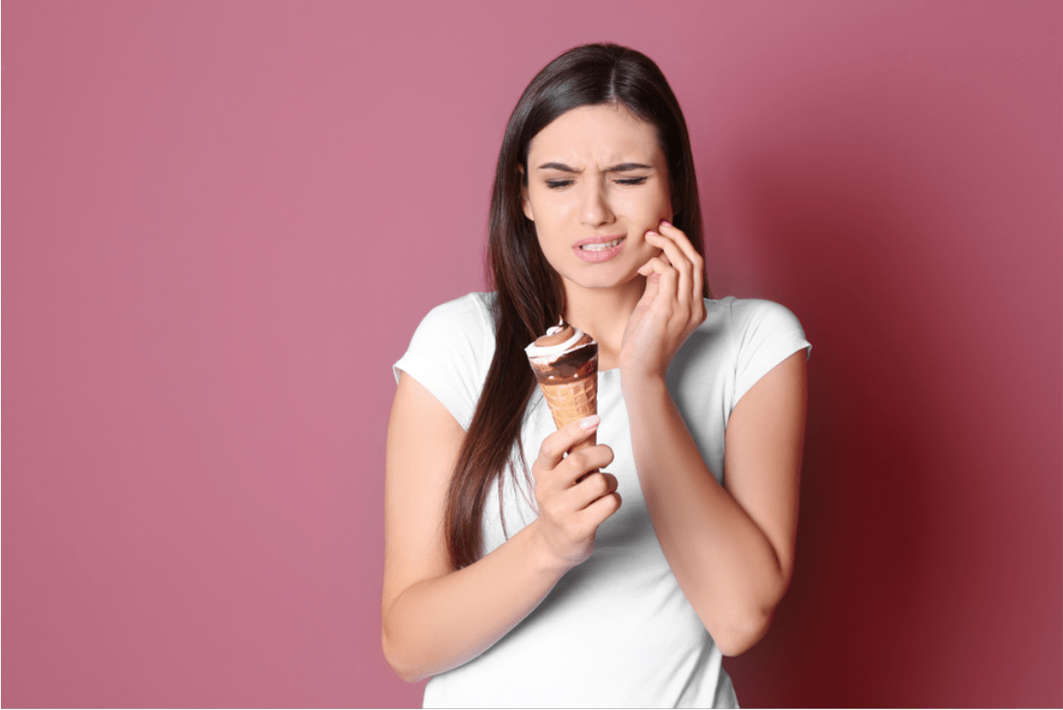 a woman wincing because of her sensitive tooth while holding a cone of ice cream