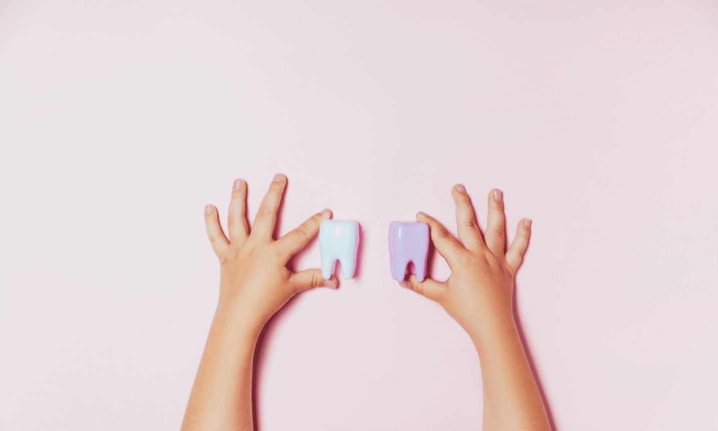 the hands of a child holding 2 mock-ups of a tooth to signify tooth decay