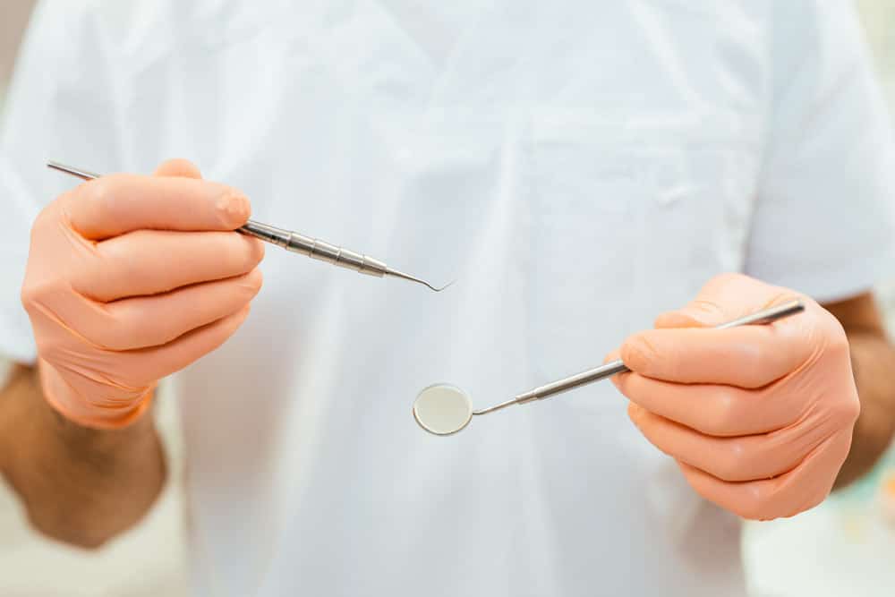 a Mona Vale dentist holding a mouth mirror and a dental probe to prepare for a root canal therapy